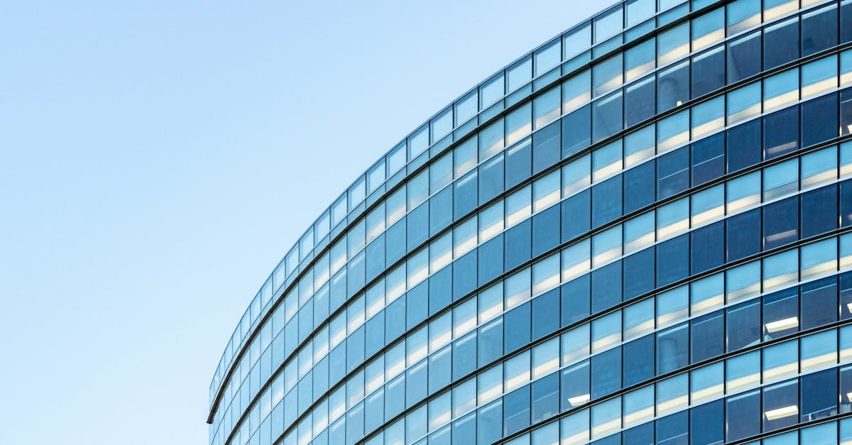 Low angle view of a modern glass office building against a clear blue sky.